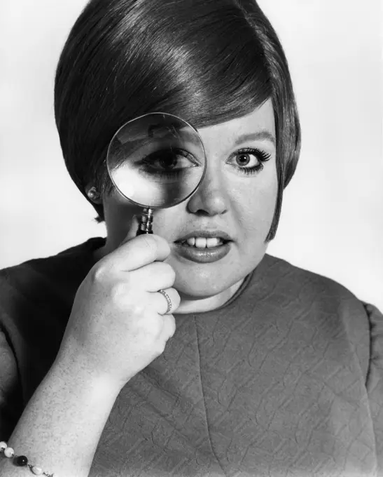 Studio portrait of teenage girl looking through magnifying glass