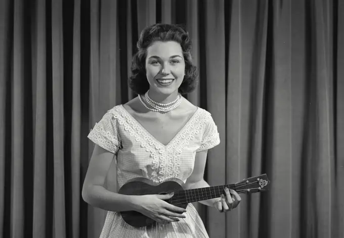 Vintage Photograph. Woman in dress and pearls playing the ukelele. Frame 1