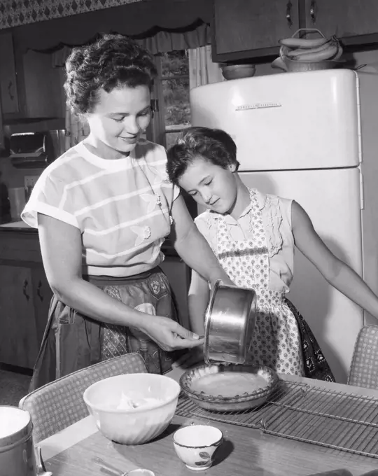 Mid adult woman preparing food with her daughter standing beside her