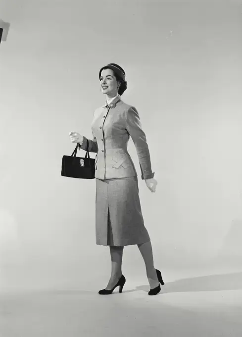 Vintage Photograph. Woman in coat with purse taking a step and smiling