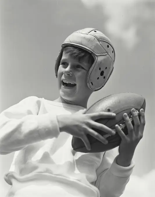 Portrait of smiling boy wearing football helmet turned to side holding up ball