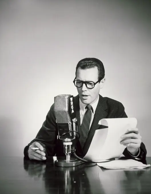 Mid adult man holding a cigarette and reading a report into a microphone