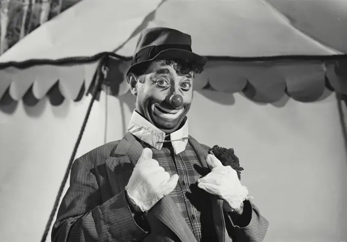 Vintage Photograph. Hobo clown smiling and holding lapels of suit in front of circus tent in background