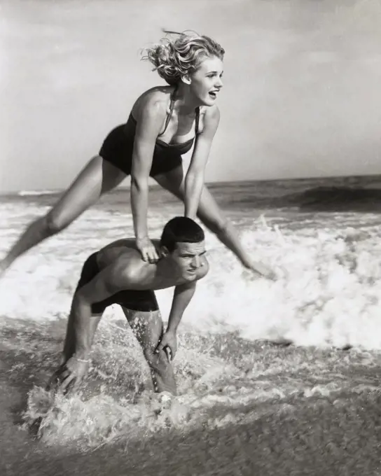 Young couple playing leapfrog in surf