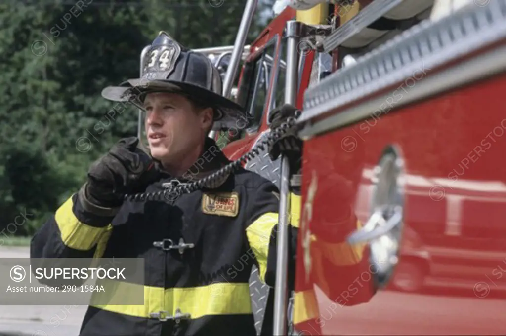 Firefighter standing near a fire engine and talking on a walkie-talkie