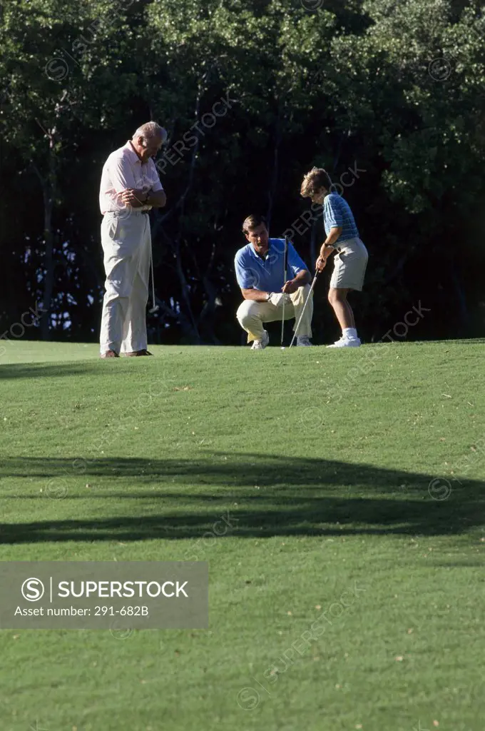 Side profile of a boy playing golf with his father and grandfather on a golf course