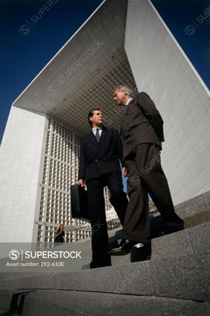 Stock Photo: 292-610E Low angle view of two businessmen moving down steps and talking to each other, La Defense, Paris, France