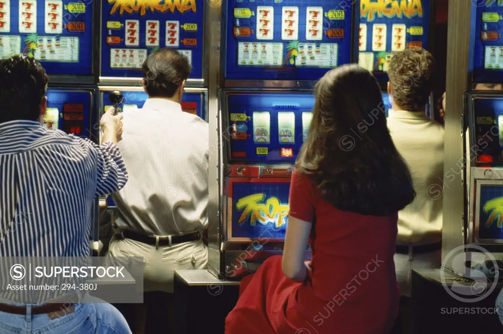 Rear view of a woman with three men playing slot machine in a casino