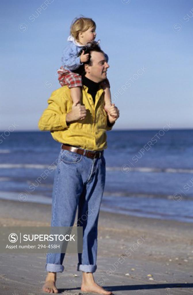 Stock Photo: 294-458H Mid adult man carrying his daughter on his shoulders and standing on the beach