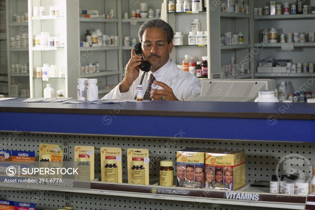 Stock Photo: 294-677A Pharmacist talking on the telephone at a checkout counter in a pharmacy