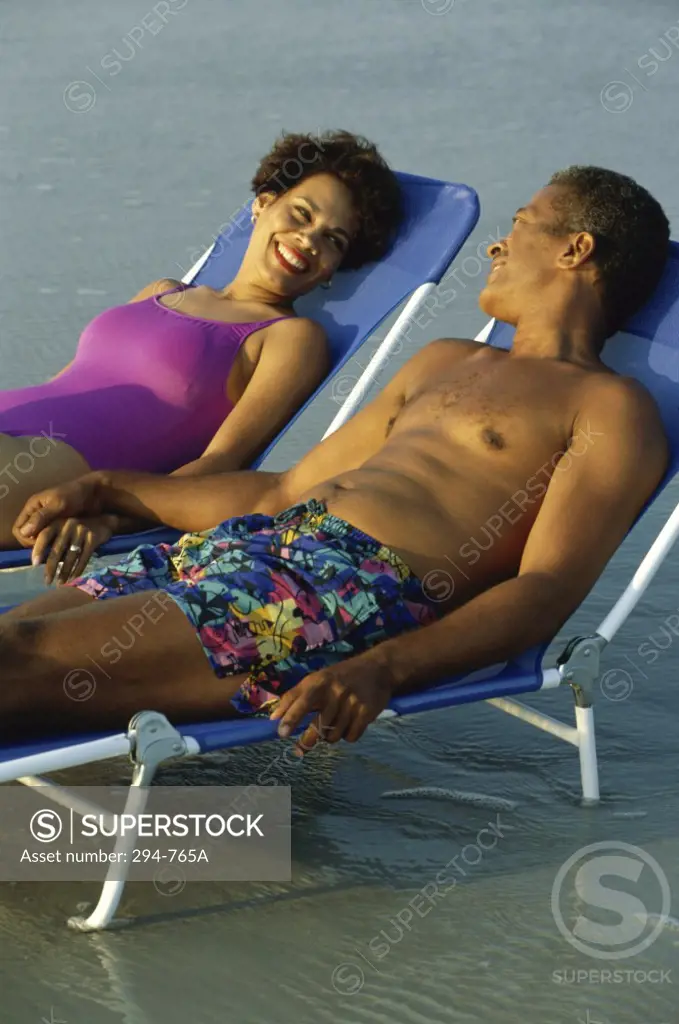 Mature couple lying in lounge chairs on the beach and smiling