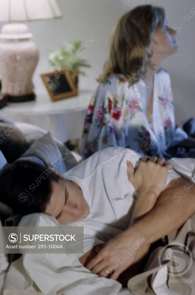 Young man sleeping with a young woman sitting beside him in the bedroom