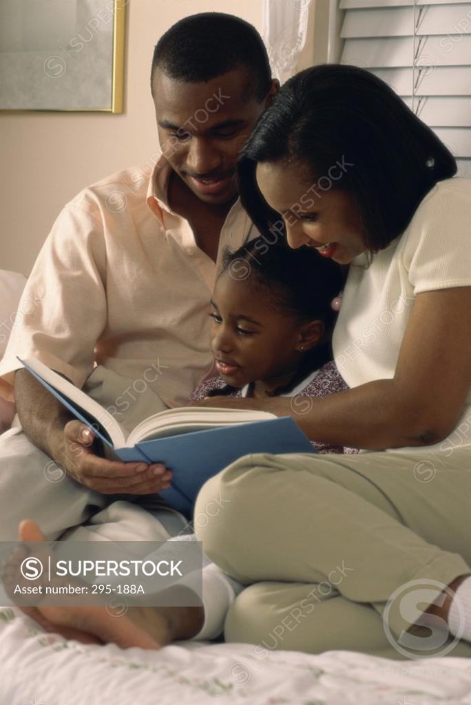 Stock Photo: 295-188A Young couple reading a book with their daughter in the bedroom