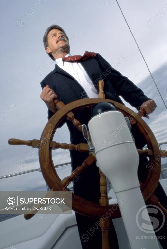 Stock Photo: 295-337K Low angle view of a businessman holding the helm of a sailing ship