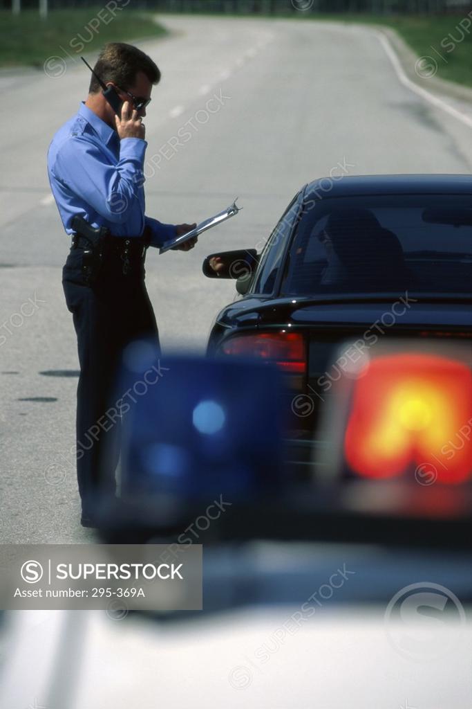 Stock Photo: 295-369A Police officer standing near a car talking on a walkie-talkie