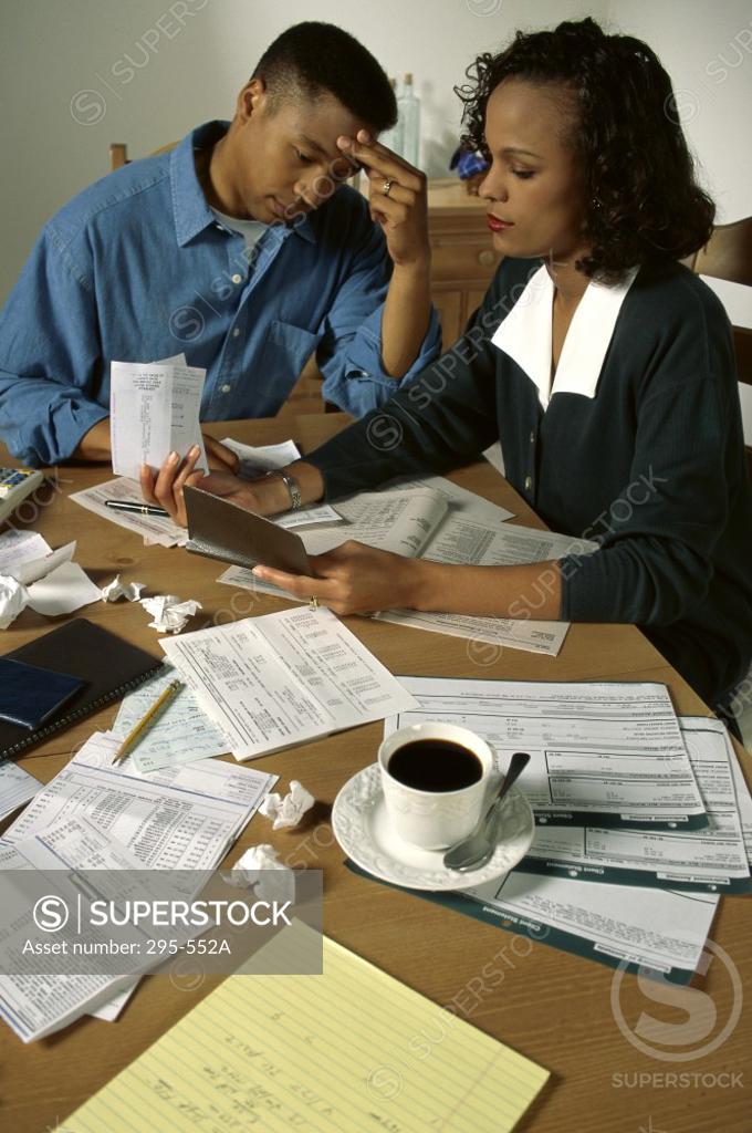 Stock Photo: 295-552A Young woman sorting out bills with a young man sitting near her