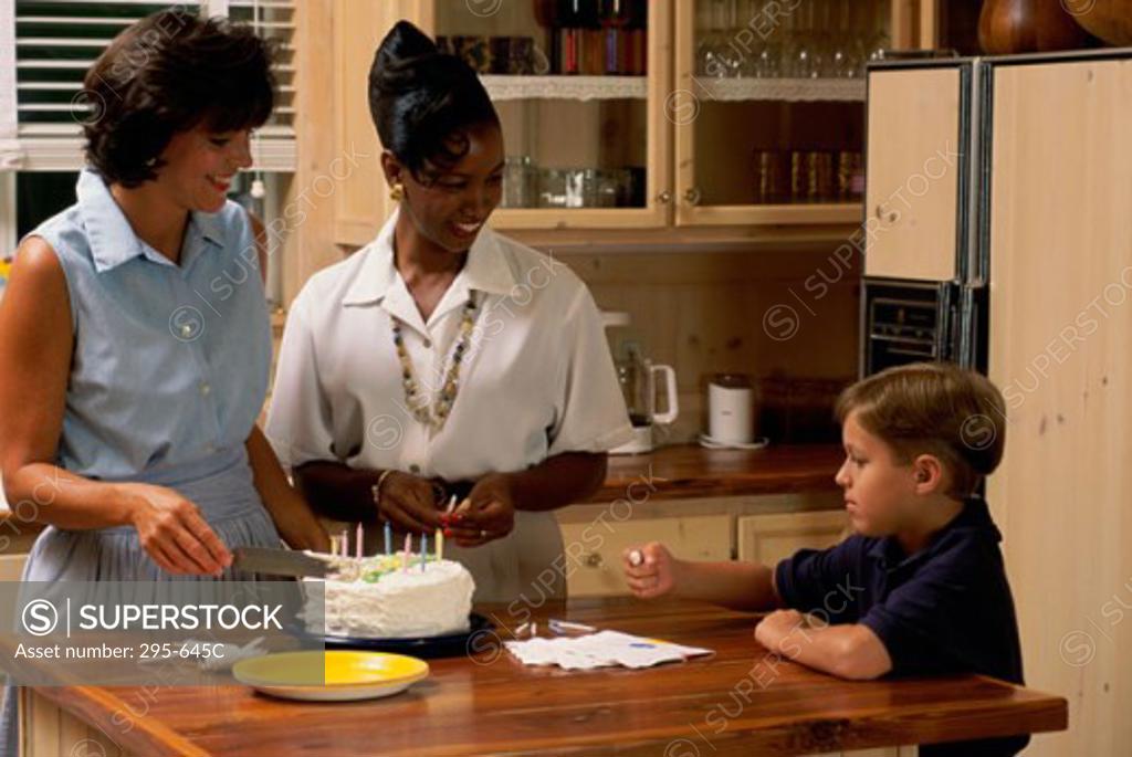 Stock Photo: 295-645C Mother cutting a cake with her son and a mid adult woman in a kitchen