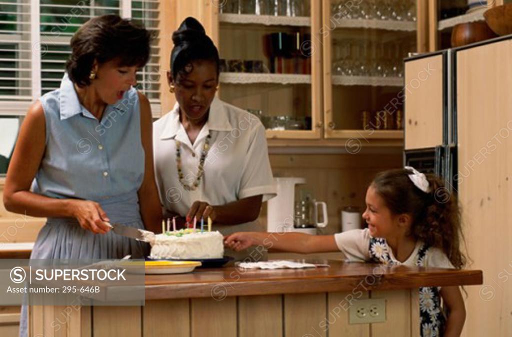 Stock Photo: 295-646B Mother cutting a cake with her daughter and a mid adult woman in a kitchen