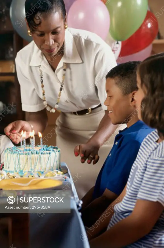 Mid adult woman lighting candles on a birthday cake in front of two children