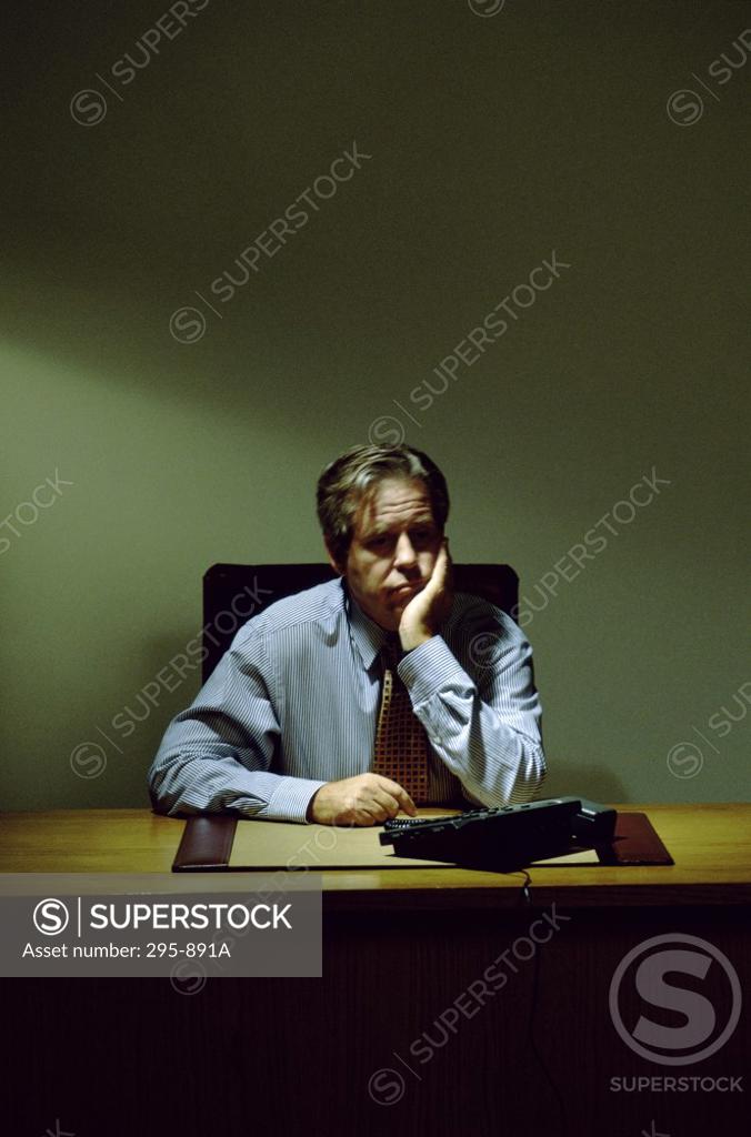 Stock Photo: 295-891A Businessman sitting at a desk with his hand on his chin