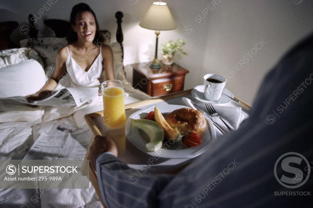 Stock Photo: 295-989A Young woman sitting on the bed and surprisingly looking at breakfast