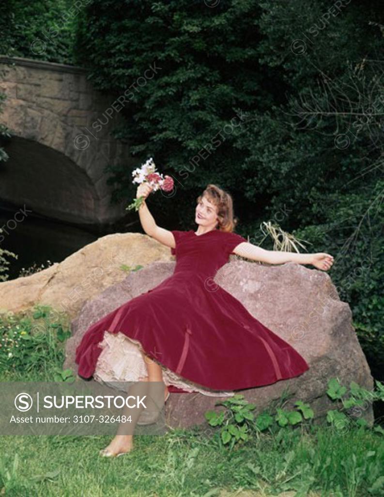 Stock Photo: 3107-326484 Young woman lying on a rock and holding a bunch of flowers
