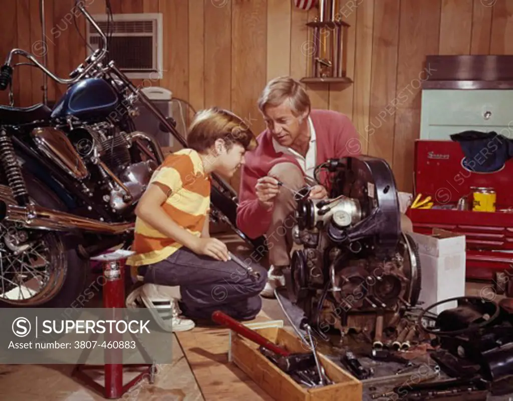 Mature man explaining an automobile engine to his son in a workshop