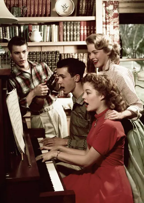 Teenage couple playing a piano with another teenage couple standing near them