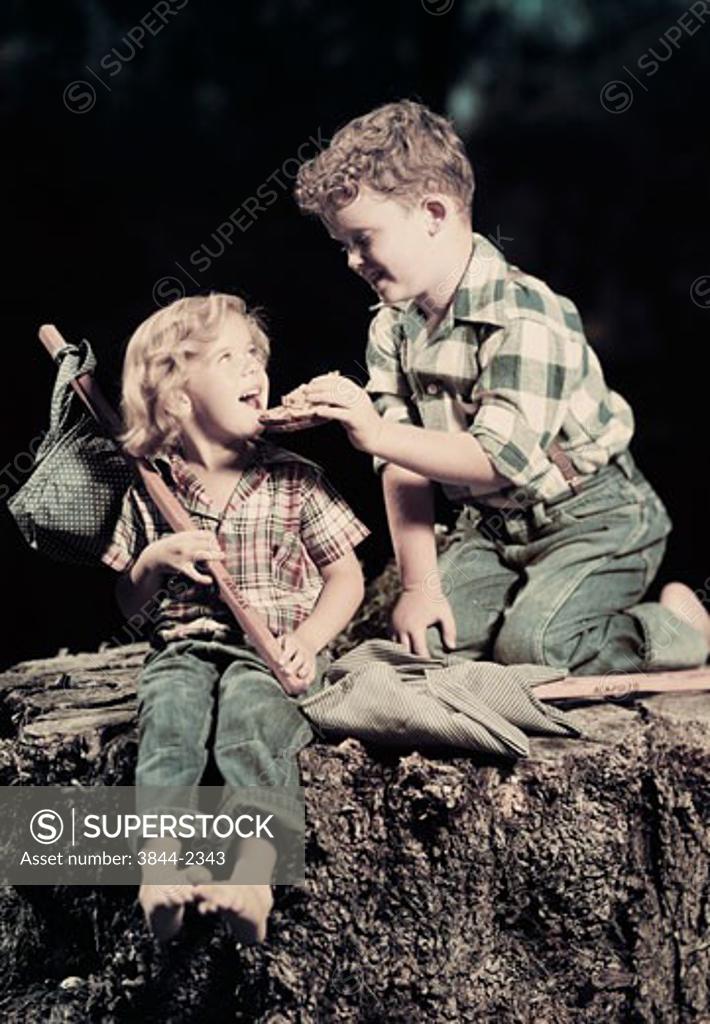 Stock Photo: 3844-2343 Side profile of a boy feeding a girl sitting on a rock