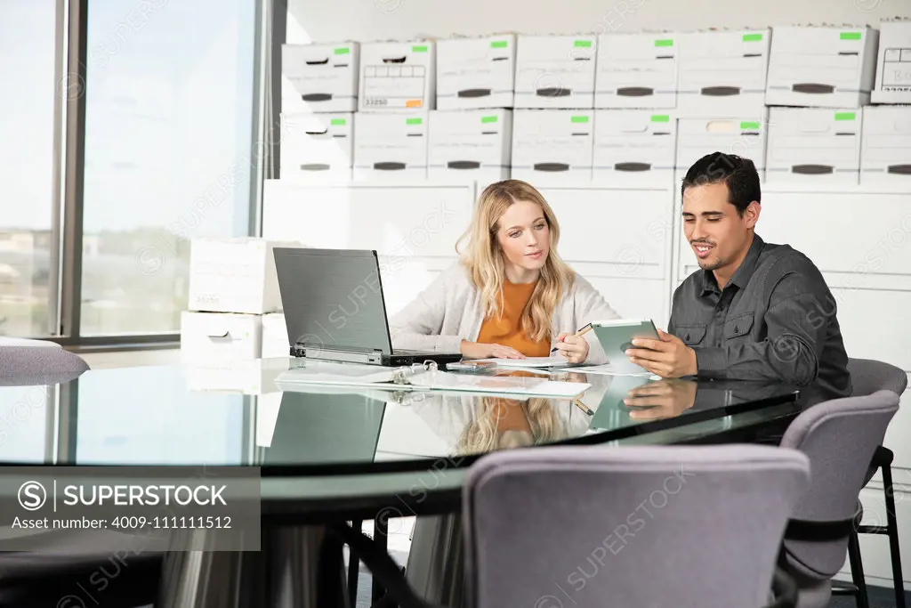 Two co-workers discuss work at a conference table in their office.
