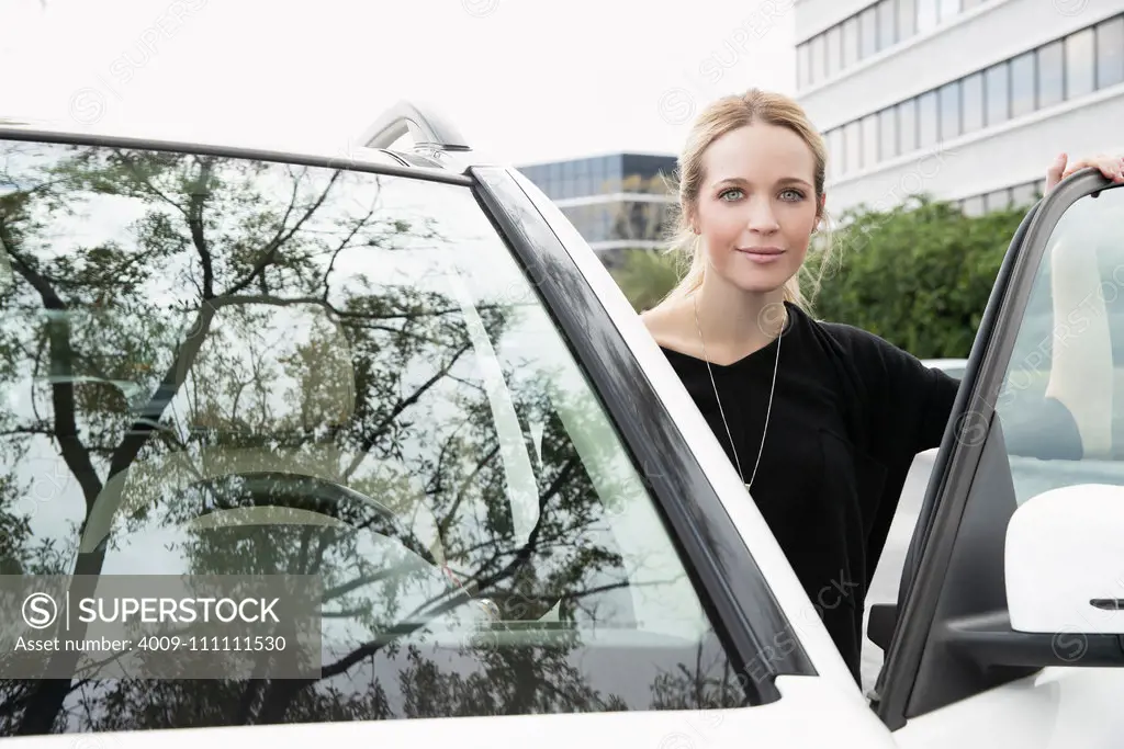 Young woman standing in the driver's door looking at camera.