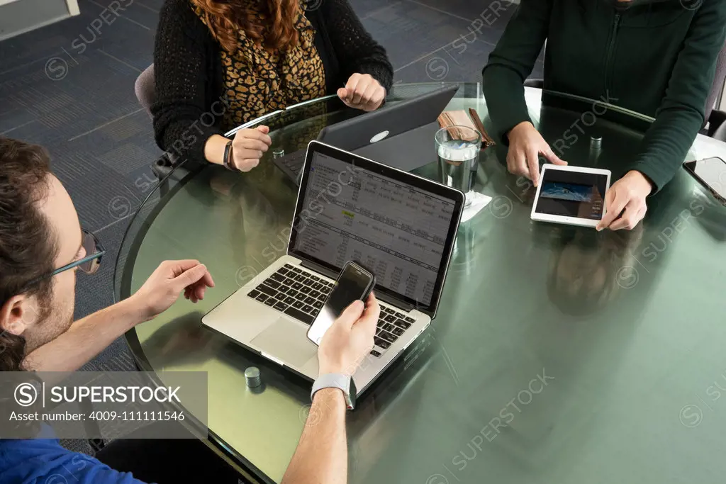 Overhead shot of three people on laptops and tablets during a meeting.