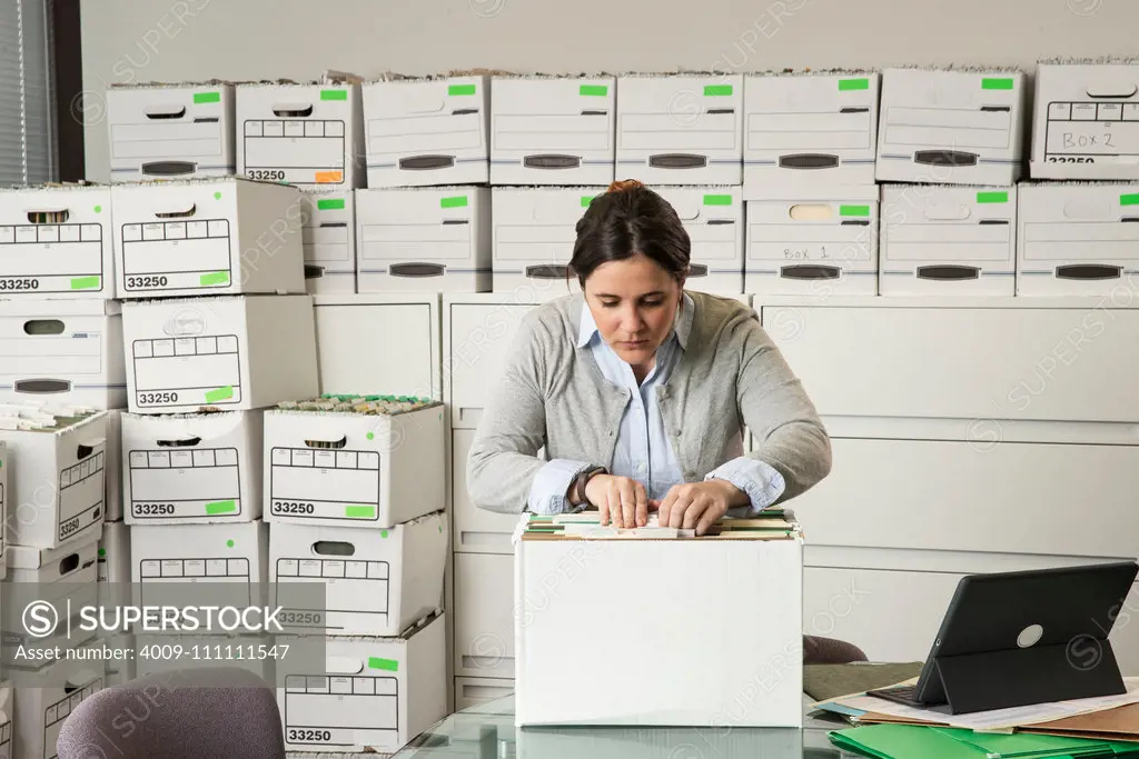 A woman looks through a box of files in an office