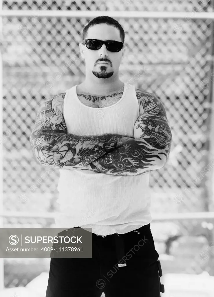 Portrait of a mid adult man standing wearing sun glasses with tattooed arms folded