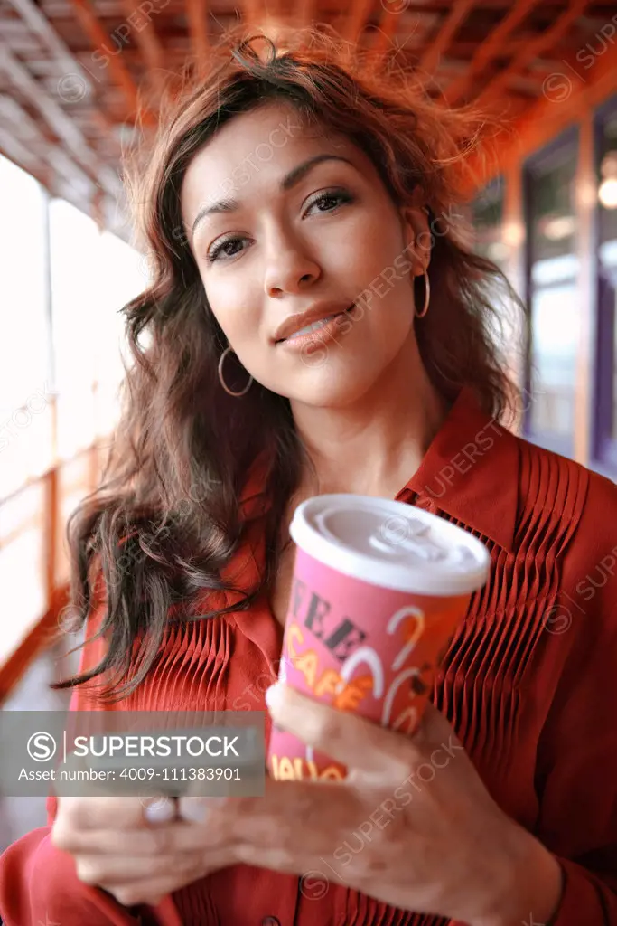 Hispanic businesswoman holding coffee and cell phone