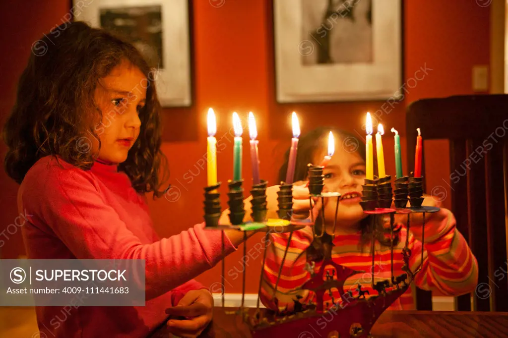 Two young girls lighting Chanukah candles.