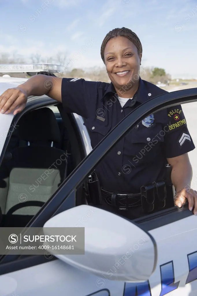 Policewoman standing in door of Police car looking towards camera smiling