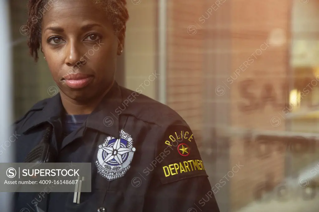 Portrait of Police woman standing in front of large glass window with reflections looking towards camera