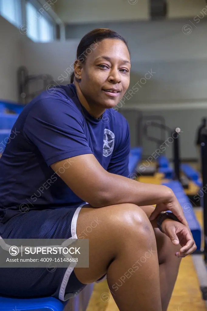 Portrait of Police woman sitting on bleachers in gymnasium looking towards camera smiling 