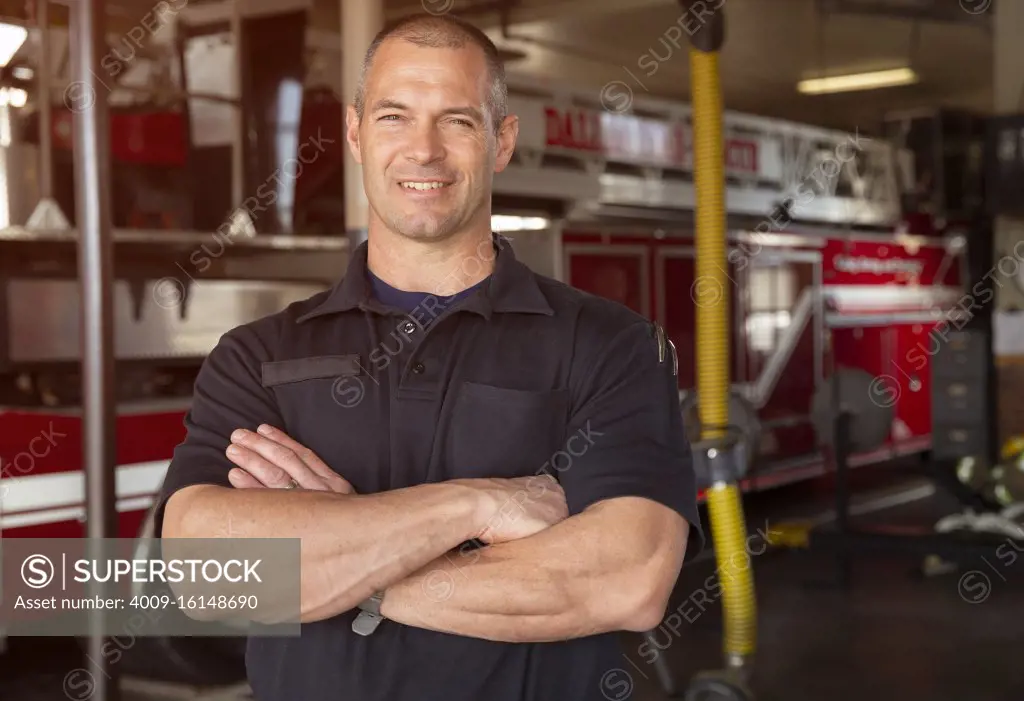 Portrait of Fireman standing in front of firetruck with arms crossed smiling 