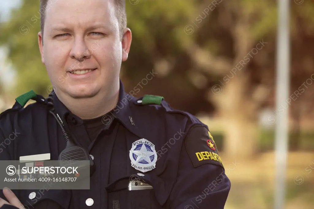 Portrait of Police officer standing outside with arms crossed looking towards camera smiling 
