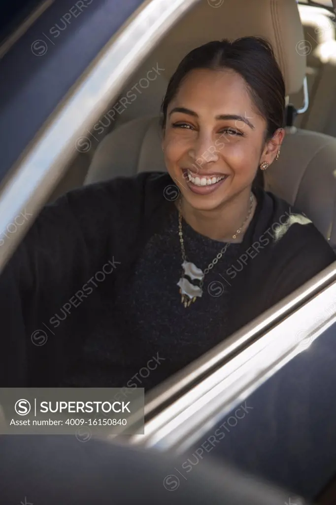 Portrait of woman sitting in drivers seat of car with window open, laughing and looking at camera 