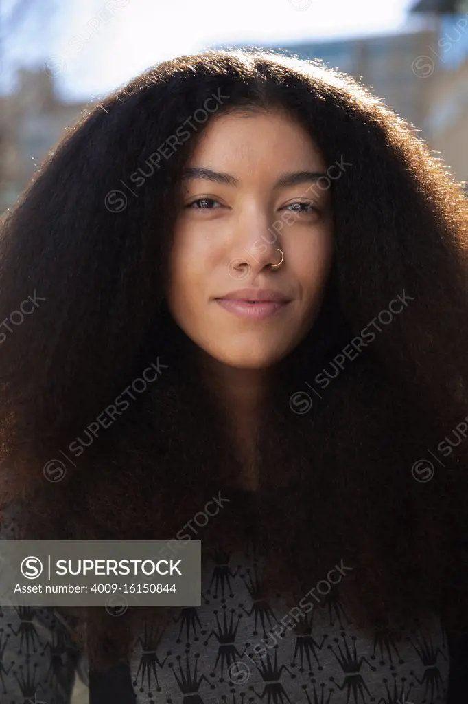 Portrait of woman with long hair standing outside, looking at camera 