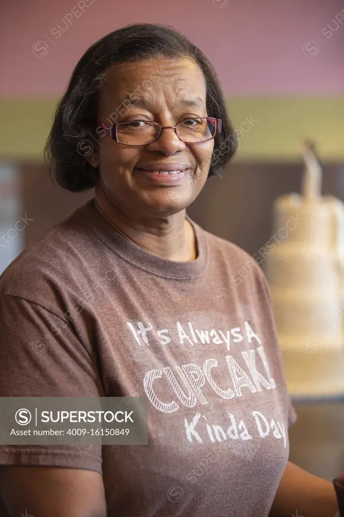 Portrait of older woman with glasses standing behind counter at bakery, smiling looking at camera 