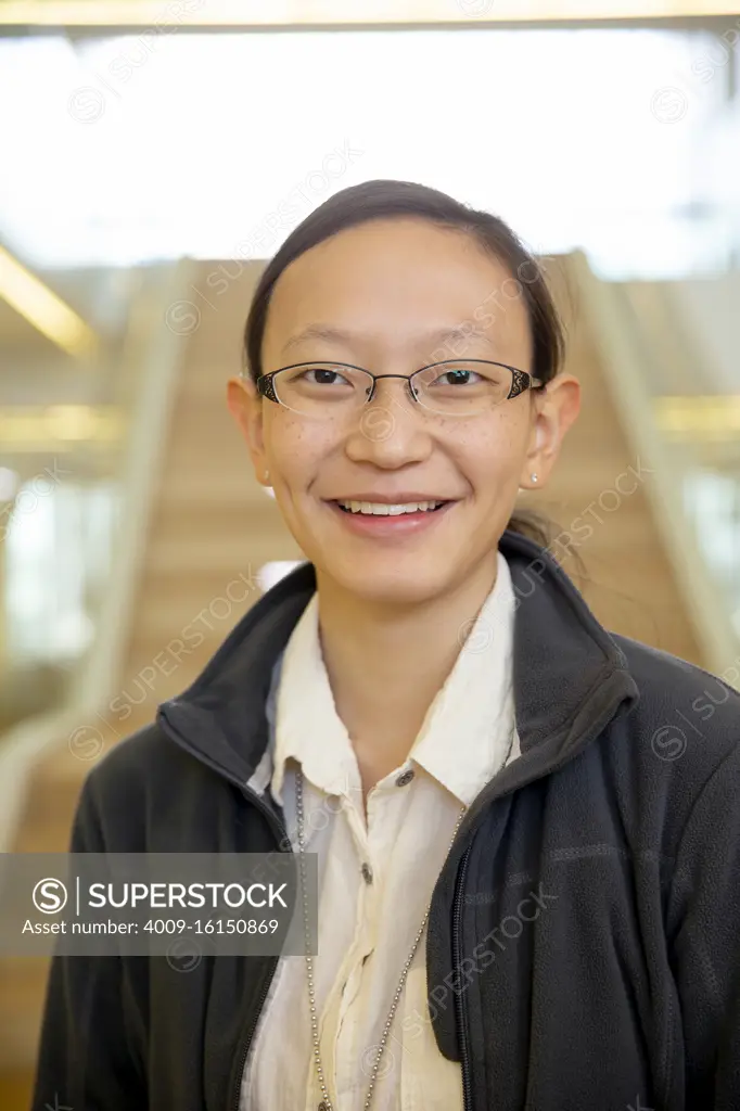 Portrait of young ethnic woman standing in lobby of building, smiling looking towards camera 