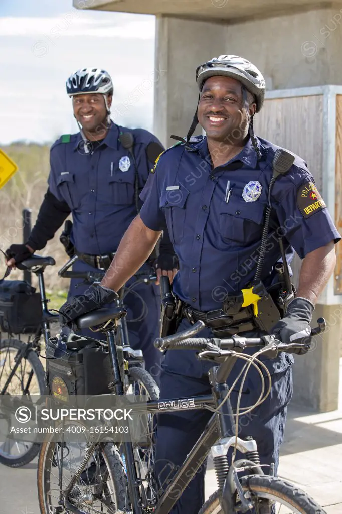 Portrait of Bicycle Police officers standing outside with their bikes looking towards camera smiling 