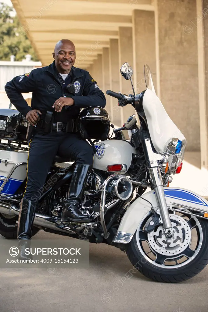 Portrait of Police officer sitting on his motorcycle outside looking towards camera smiling 