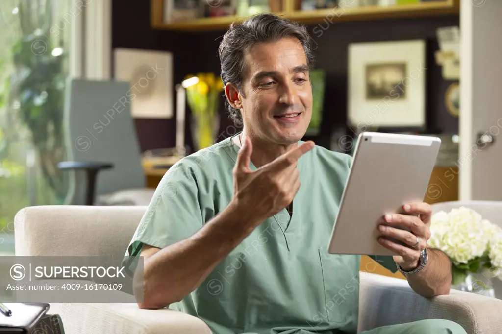 Hispanic Male doctor practicing tele-medicine from his home office, Talking to patient via video call on tablet 