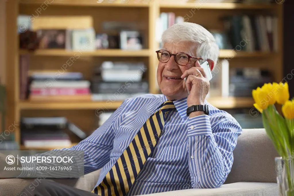 Senior Caucasian doctor practicing tele-medicine from his home office, Talking to patient on telephone