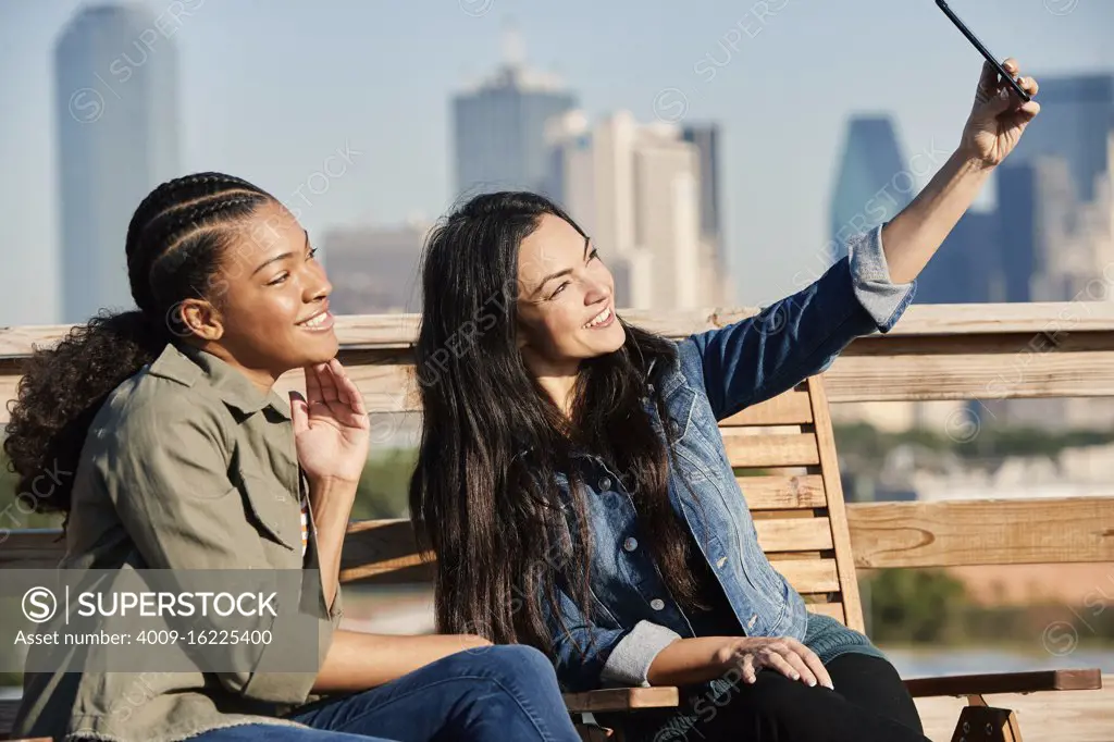 Group of young co-workers hanging out on rooftop patio, two women taking selfie with mobile phone 